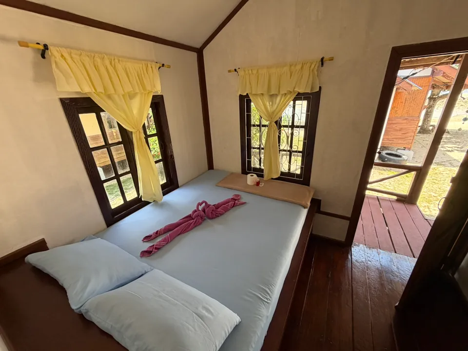 Inside the garden bungalow: a double bed between two curtained windows, with the balcony door open